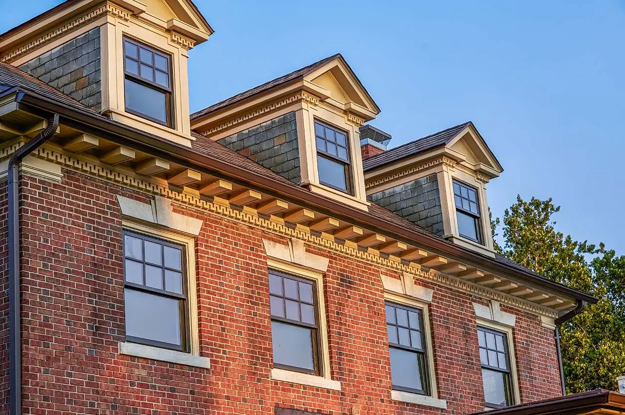 revive__bronze_claddh_ds_pocket_windows_buildertbd_kansascity_mo_2018_35_coami4jtahc1g1ja1bff56-1280x850 lose-up view of the upper section of a brick building featuring multiple dormer windows with white trim